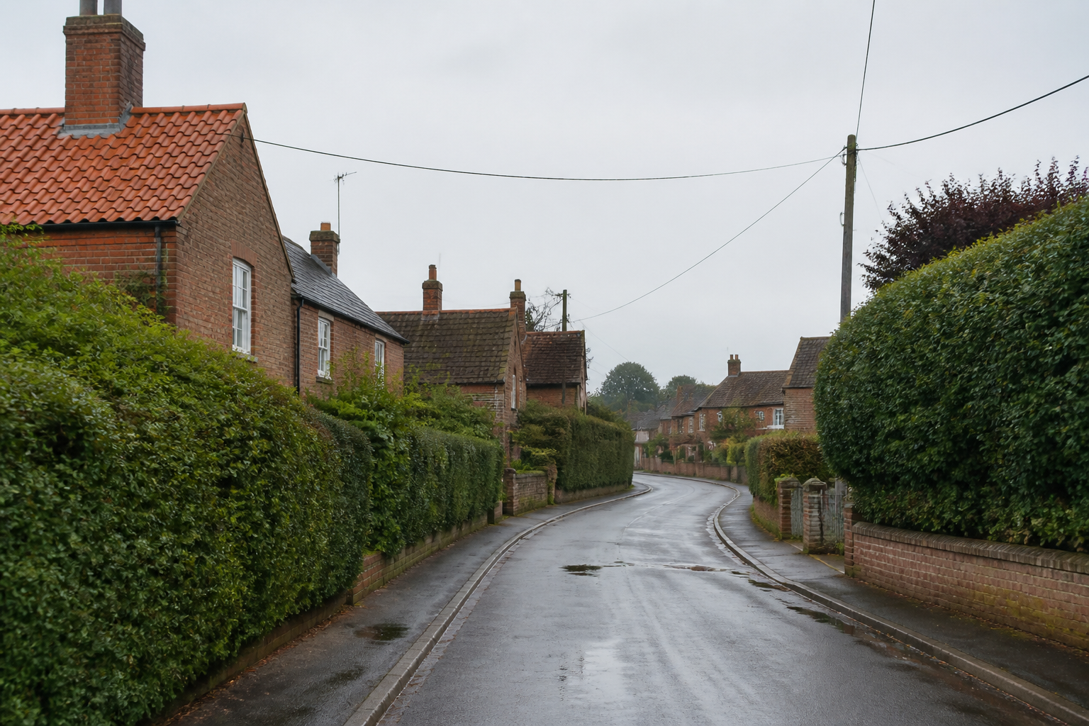A quiet village street of brick cottages and hedges, with no shop fascia