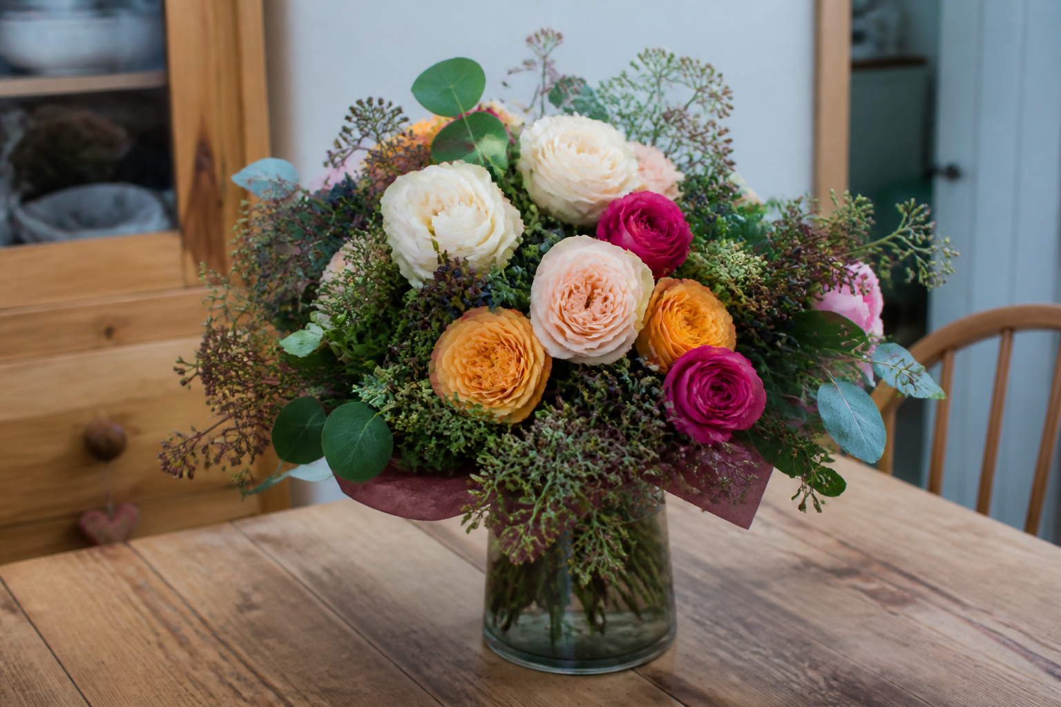 A mixed seasonal bouquet on a wooden kitchen table, with no shopfront and no price tickets