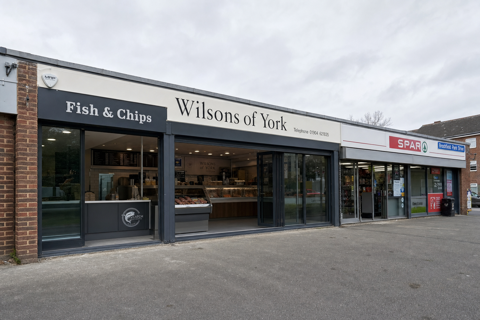 Wilsons of York on Brockfield Park Drive: dark-brick parade, cream fascia in black serif, shopfront open in daylight