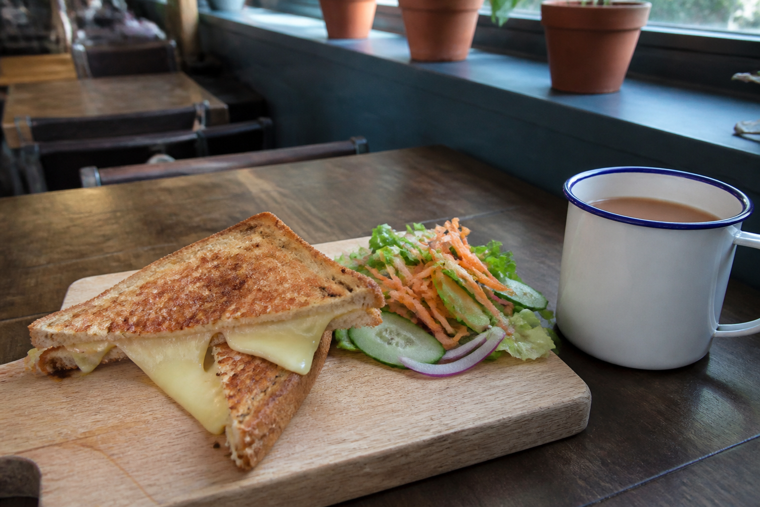 A toasted sandwich on a board with a side salad and a mug of tea