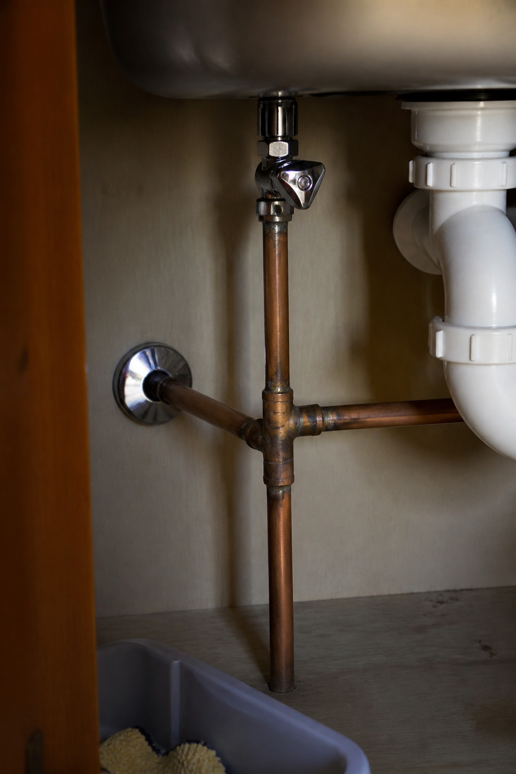 Copper pipework and a stopcock under a British kitchen sink, with no brand names